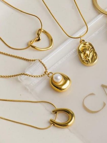 A collection of minimalist gold pendants and necklaces arranged on a branded plate. This clean, organized flatlay is excellent for showcasing the variety within a product line.