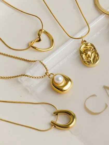 A collection of minimalist gold pendants and necklaces arranged on a branded plate. This clean, organized flatlay is excellent for showcasing the variety within a product line.