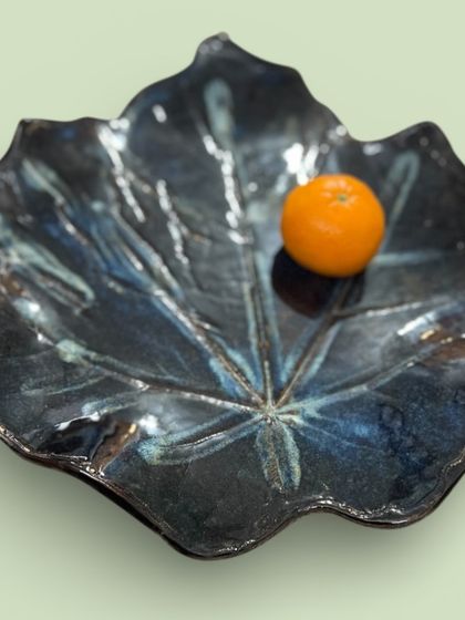 Another view of the large, leaf-shaped platter, showing how the glaze pools and breaks over the texture. The single orange provides a sense of scale for this unique, nature-inspired centerpiece.