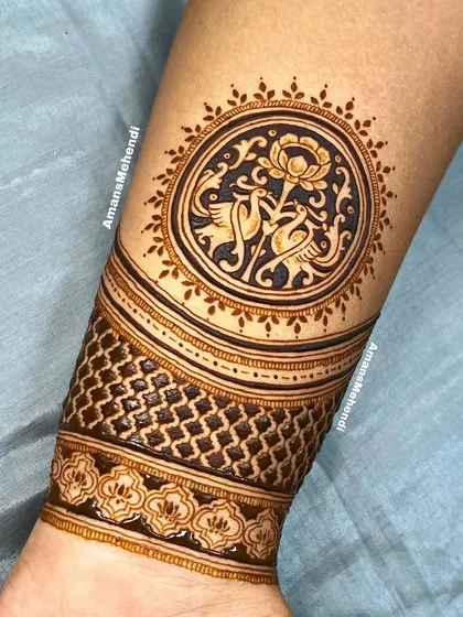 This wrist cuff combines a circular motif of peacocks and a lotus with a geometric checkered band, blending figurative and abstract patterns.