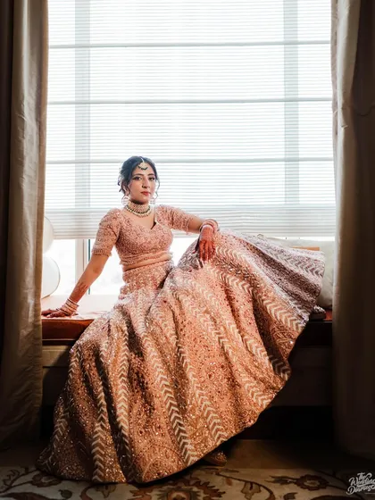 A beautiful bridal portrait, with the bride seated by a window. The soft, natural light and the elegant spread of her pastel lehenga create a picture of pure grace.