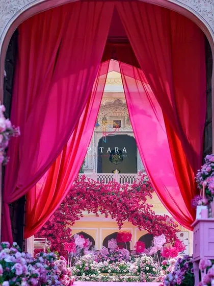 A beautifully framed shot of the floral arch, seen through the main entrance drapes. This perspective emphasizes the depth and layers of the decor, creating an inviting and majestic welcome.