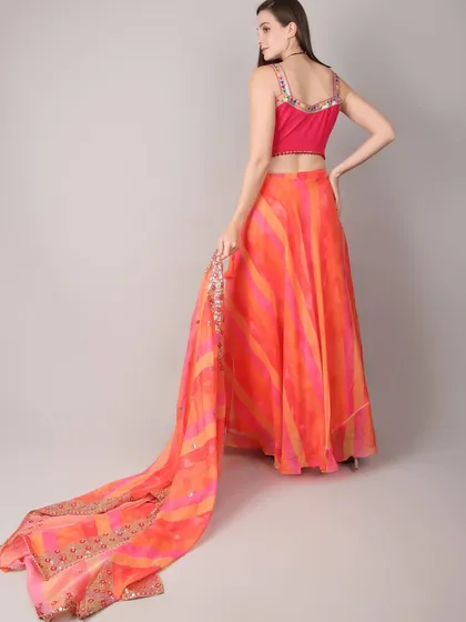 The back view of the orange lehenga shows the delicate straps of the blouse and the beautiful, long drape of the leheriya-style dupatta with its sequined border.