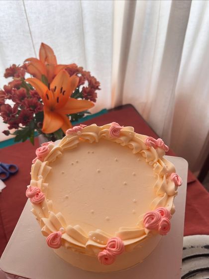 A simple and sweet cake with a peach-colored buttercream base, decorated with a border of piped pink roses.