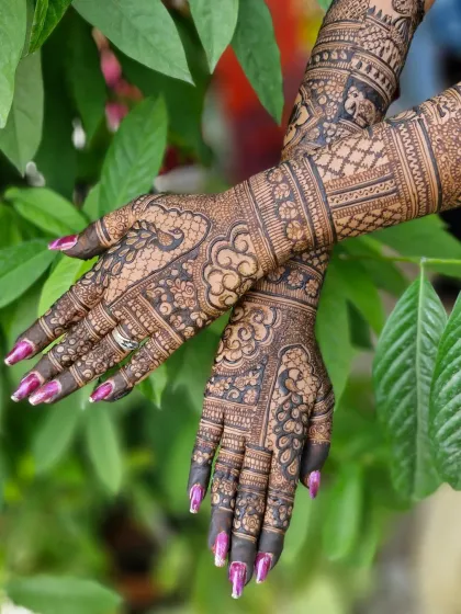 The crossed-hands pose showcases the symmetry and flow of the traditional peacock and floral mehendi design.