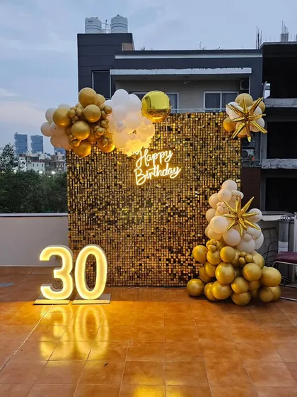 A stunning 30th birthday setup on a rooftop, featuring a gold sequin wall, a neon sign, and light-up numbers against the city skyline.