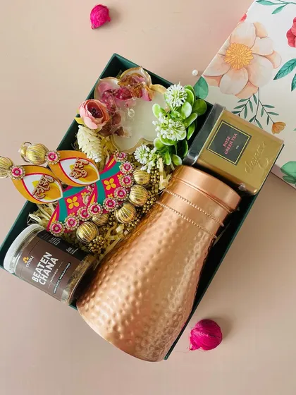 An angled view of the floral hamper, showing the rich contents like the copper bottle and "Shubh Labh" hangings, perfect for bringing festive cheer.