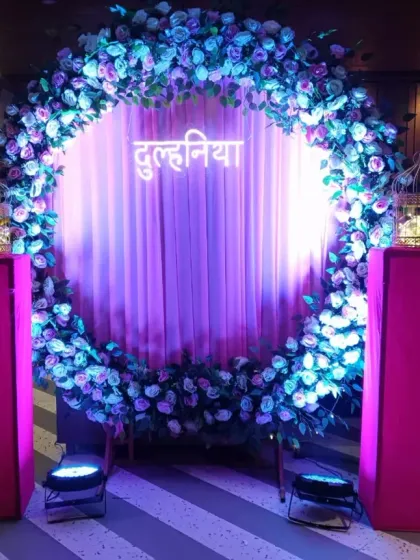 A stunning circular floral arch with a "दुलहनिया" (Bride) sign in the center. The purple and blue lighting gives this engagement or sangeet backdrop a vibrant, celebratory feel.