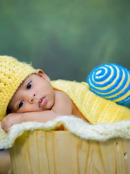 A sweet newborn in our snail costume, looking right at the camera from a wooden bucket. This pose is great for capturing their beautiful, curious eyes.