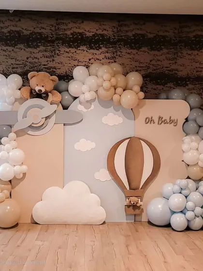 An "Oh Baby" setup with a hot air balloon and airplane theme. The backdrop creates a sky full of clouds made from balloons, with wooden cutouts of a plane and hot air balloon for a vintage adventure feel.