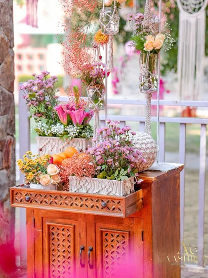 A charming wooden cabinet with carved details, used as a stand for a variety of beautiful floral arrangements in rustic and macrame vases.