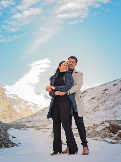 A happy, bright shot of a couple embracing under a clear blue sky in a snowy location.