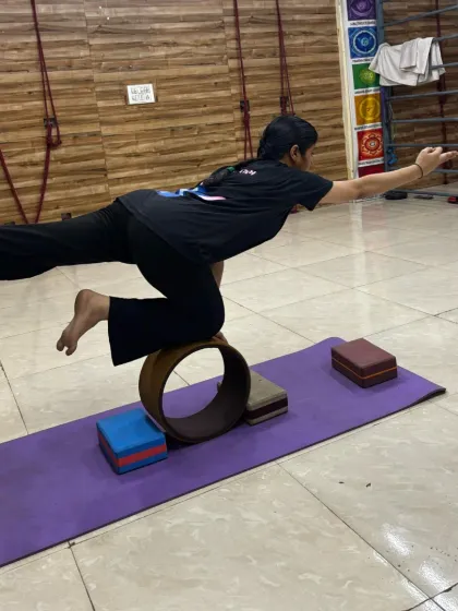 A student practices a variation of Virabhadrasana III (Warrior III) while balancing on a yoga wheel, adding a significant challenge to a classic pose.