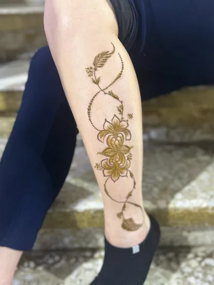 An elegant vine design that wraps around the leg in an infinity loop. This infinity henna tattoo style incorporates delicate flowers and feathers for a modern and symbolic look.