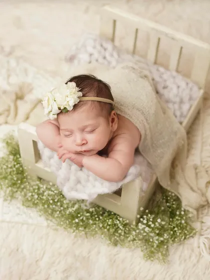 This newborn is nestled in a tiny bed, surrounded by baby's breath. The natural textures and soft lighting create a serene and organic feel for this baby portrait.