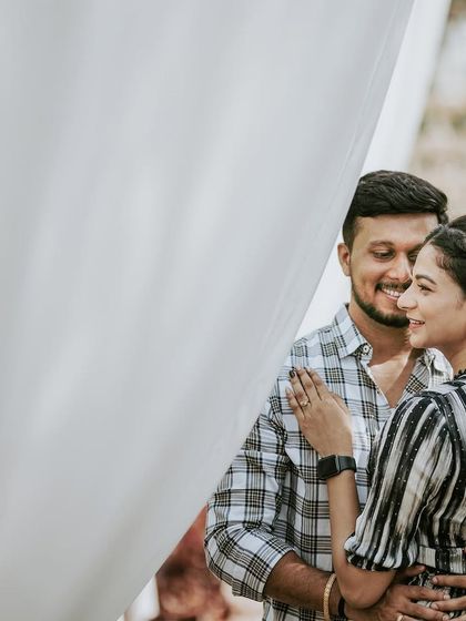 A sweet, intimate moment of a couple during their picnic-themed pre-wedding shoot, framed by soft white fabric.