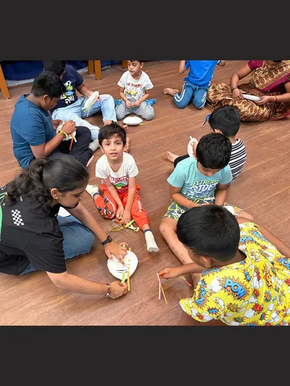 An instructor demonstrates a step in making a paper plate basket to a group of attentive children. We provide clear, step-by-step guidance to ensure every student can participate and feel successful.