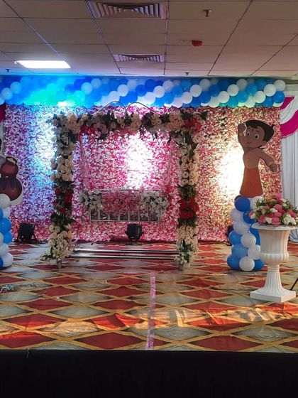 A naming ceremony stage with a Chhota Bheem theme. The cradle is placed under a floral arch against a beautiful flower wall backdrop.