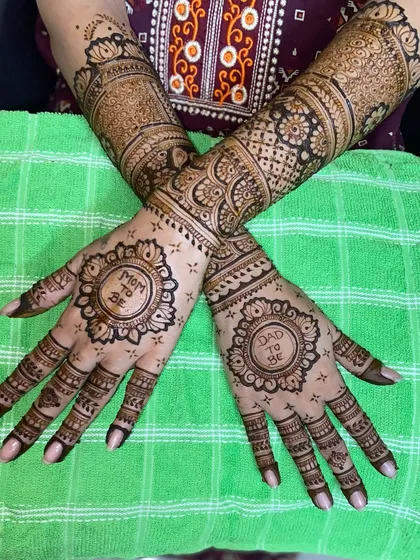 A classic baby shower mehandi with 'Mom to Be' and 'Dad to Be' inscribed within beautiful circular frames, surrounded by traditional patterns extending up the arm.