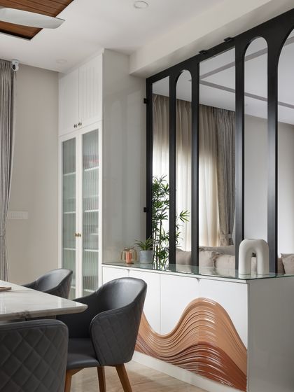 This custom console table is a centerpiece, featuring a unique wavy design on the shutters created with layered, colored panels. It sits below an elegant arched metal partition that separates the dining and living areas without closing them off.