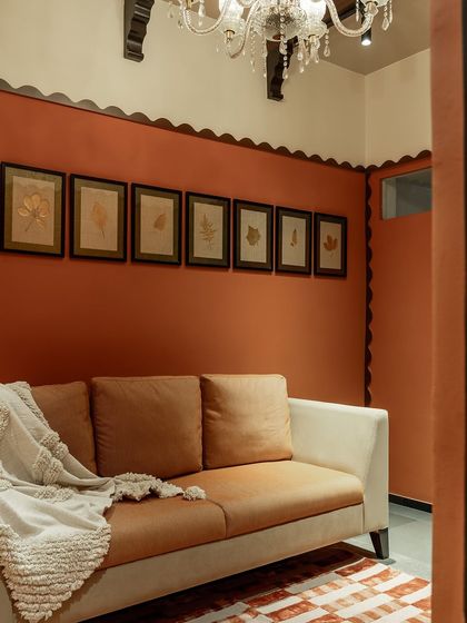 A simple, modern sofa with tan upholstery, accented with a cozy throw blanket. The room is painted in a warm terracotta, with a gallery wall of pressed botanicals, creating an earthy and inviting atmosphere.