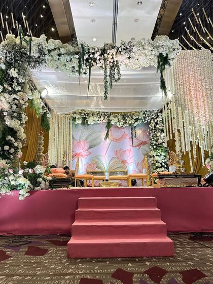 An elegant mandap featuring a lotus-print backdrop and a canopy of white and green florals. The design incorporates traditional elements like hanging jasmine strings, creating a serene and sophisticated space for the wedding rituals.