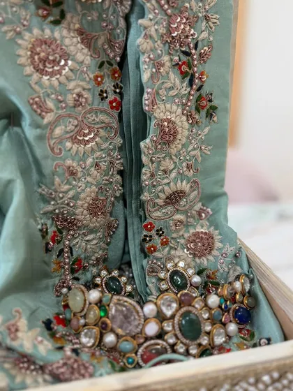 A close-up of the intricate, multi-colored embroidery and beadwork on a mint green outfit, paired with a statement necklace.