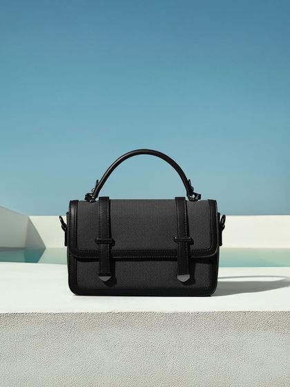 A sleek black handbag shot in a minimalist, architectural setting with a pool in the background. This creates a feeling of modern luxury and clean design.