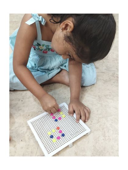 A child carefully places pegs into the board, demonstrating concentration and developing the pincer grasp essential for future writing skills.
