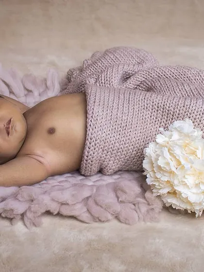 A simple and natural pose showing a sleeping newborn partially covered by a soft knitted blanket. This style focuses purely on the baby's delicate features.