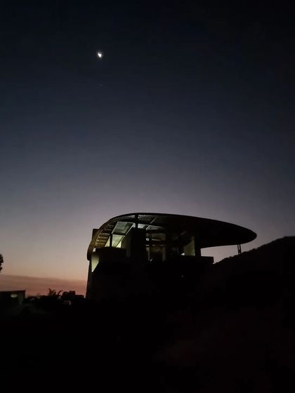 In the quiet of the evening, the unfinished structure of the Soma house stands as a beacon by the foothill. This image captures the promise of the space, a shelter designed to embrace both the earth and the night sky.