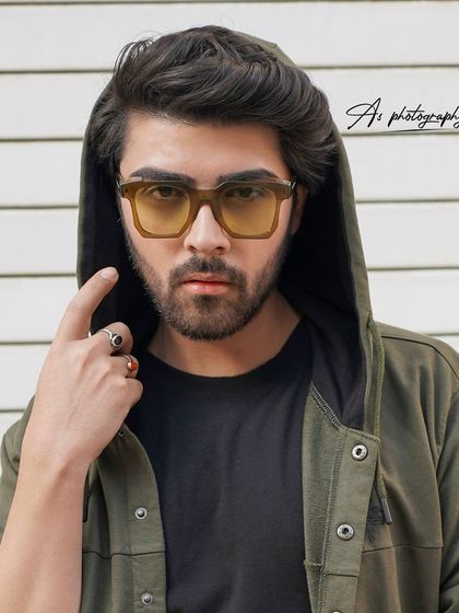 A street style portrait featuring a model in a hooded jacket and tinted glasses. The direct gaze and confident pose make this a strong image for a fashion influencer's profile.
