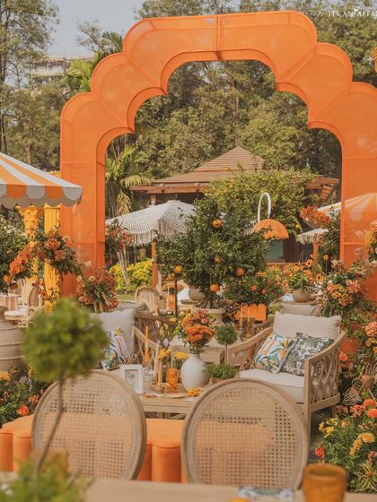 A view through a vibrant orange arch, revealing a cozy seating area with cane furniture and lush orange florals.