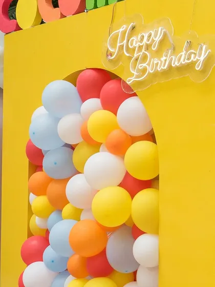Cocomelon is every child's fantasy. This close-up shows a detail from a Cocomelon-themed party, featuring a 'Happy Birthday' neon sign and a colorful balloon-filled arch.