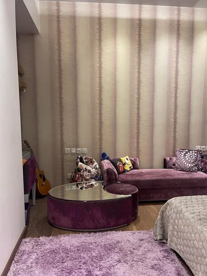 The seating area in this bedroom features a plush purple chaise lounge and a unique mirrored coffee table. This corner is designed for relaxation, adding a touch of glamour and personality to the space.