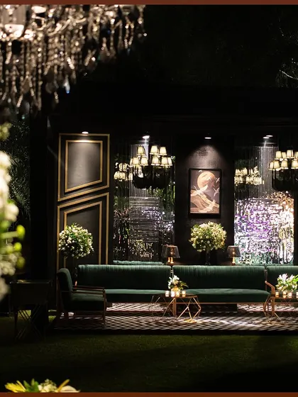 A lounge setup for a cocktail night, featuring deep green velvet sofas against a modern, geometric backdrop. The lighting and floral arrangements add softness to the contemporary design.