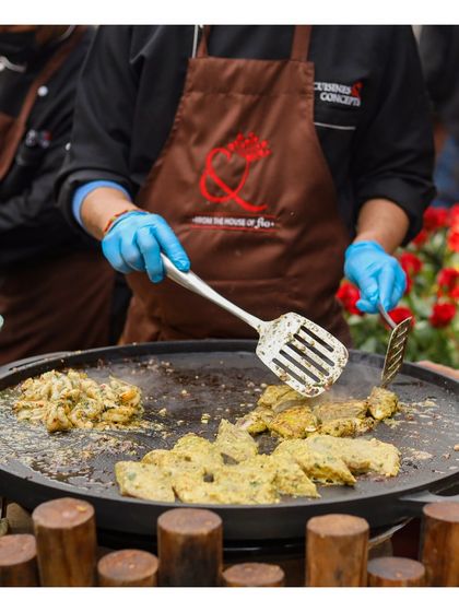 A chef uses a spatula to turn pieces of marinated paneer or chicken on a large, round tawa. The vibrant yellow marinade and fresh ingredients showcase the colourful and flavourful nature of our live Indian cooking stations.
