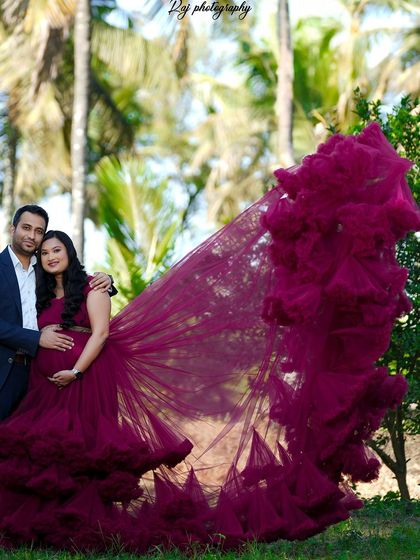 A dramatic outdoor portrait featuring a wine-colored ruffled gown with a long train. The lush green background makes the color of the dress pop.