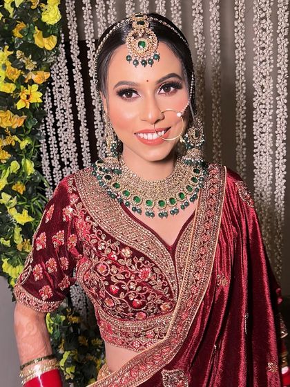 My beautiful bride Pratibha, smiling brightly. We chose a deep maroon velvet lehenga and paired it with soft, shimmery makeup and emerald green jewelry for a regal look.
