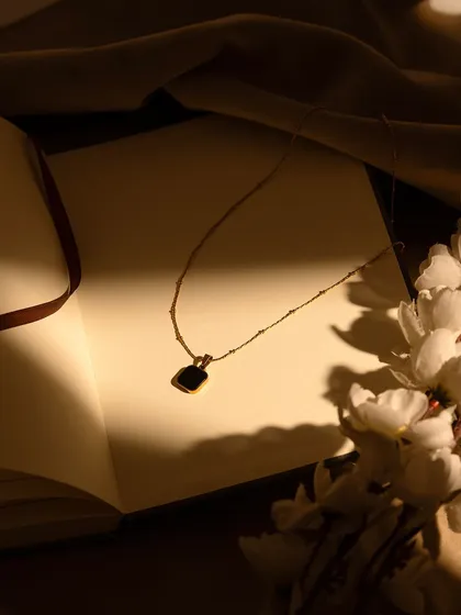 An atmospheric shot of a delicate gold necklace resting on an open book. The soft, focused light creates a warm, intimate, and romantic mood, perfect for fine jewelry.