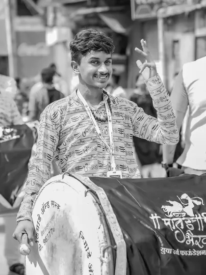 A black and white portrait of a smiling young dhol player.