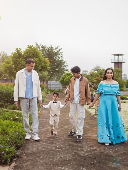A family of four, including two sons of different ages, holds hands while walking along a path in a park. This shot captures a quiet, connected moment during a family outing.