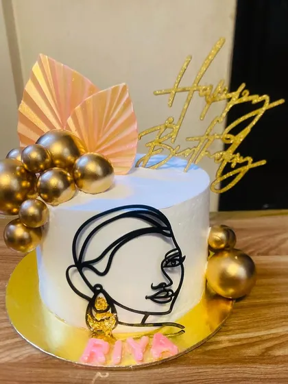 A chic and modern cake with a line-art face and gold accents.
