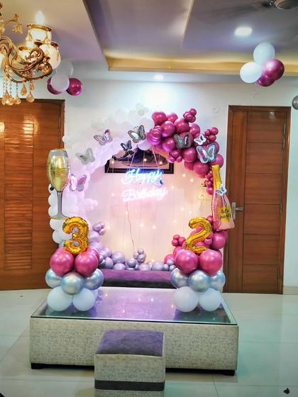 A sophisticated 32nd birthday decoration at home. The setup includes a circular backdrop with pink and silver balloons, butterfly accents, and large number foil balloons, all elegantly arranged around a glass table.