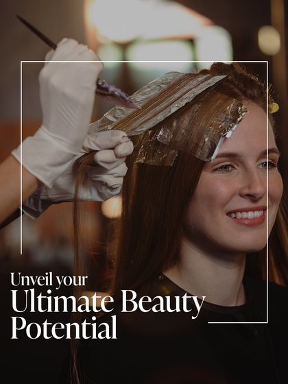 Unveil your ultimate beauty potential. A client smiles as our colorist applies a new hue, a process that promises to transform her look and elevate her style.