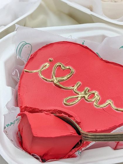 A close-up of our red heart-shaped "I love you" bento cake. The rich red frosting and delicate gold lettering make it a beautiful and delicious gift.