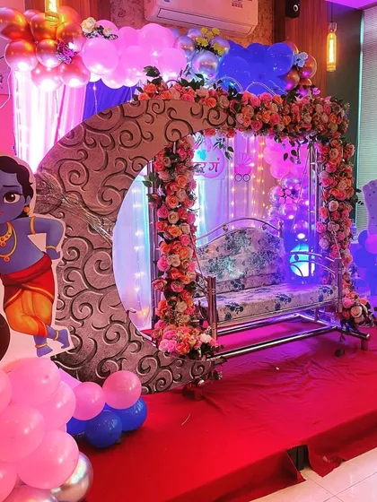A baby shower setup featuring a decorated cradle, a floral moon arch, and a cutout of little Krishna.