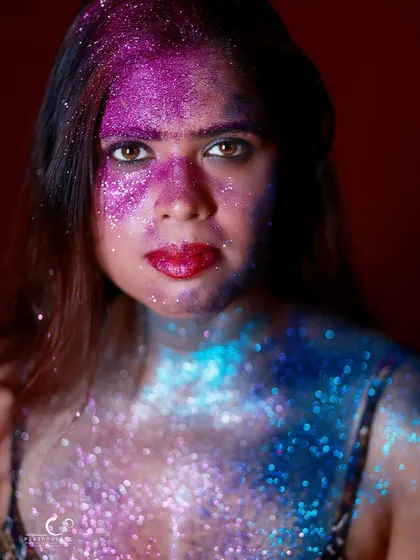A powerful and direct portrait, adorned in a galaxy of blue and purple glitter. Her gaze is steady and confident, owning the artistic and bold look.