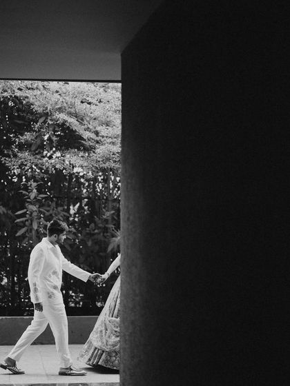 An artistic black and white shot of the couple walking hand-in-hand. The strong architectural lines and shadows create a modern and timeless feel.