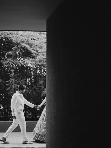 An artistic black and white shot of the couple walking hand-in-hand. The strong architectural lines and shadows create a modern and timeless feel.